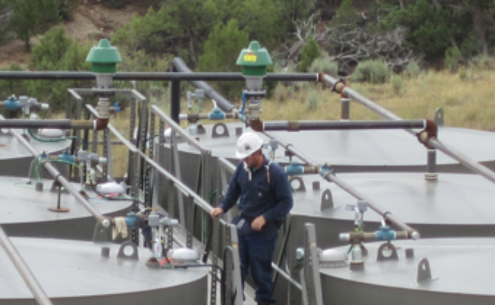 Worker preparing to gauge oil production tanks.